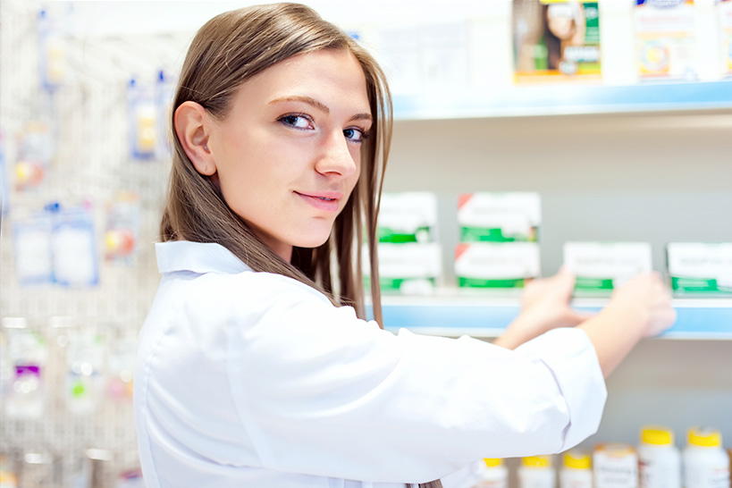 Young female pharmacy technician straightens medications on shelves.