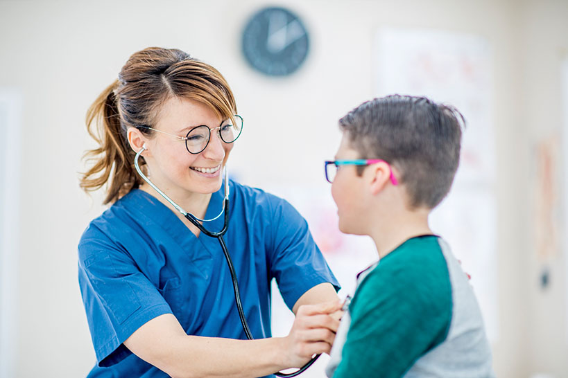 Young female medical assistant checks child patient heartbeat