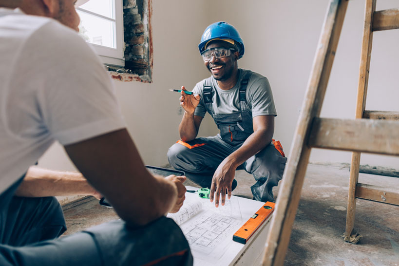 Construction worker in hardhat discusses blueprints with co-worker.