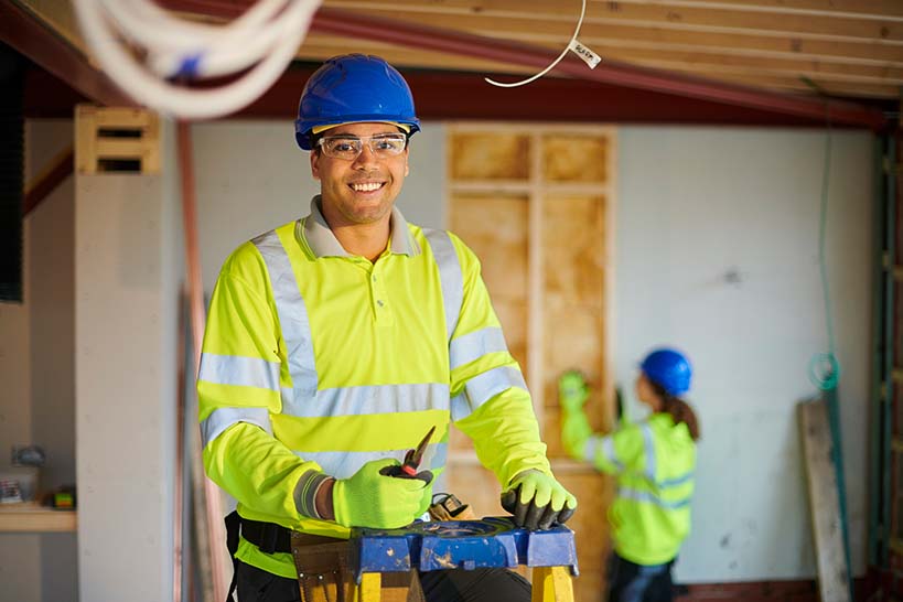 Electrical technician smiles at camera while standing on a ladder.