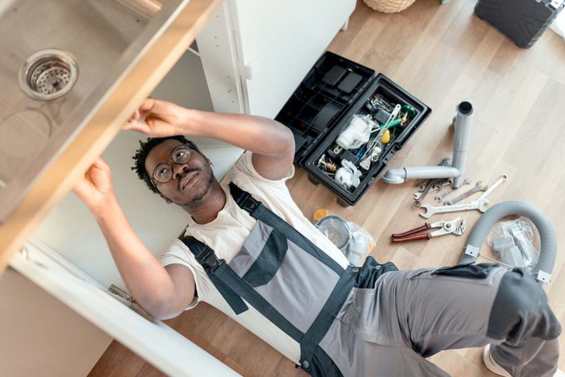 Plumbing technician laying down to repair a sink.